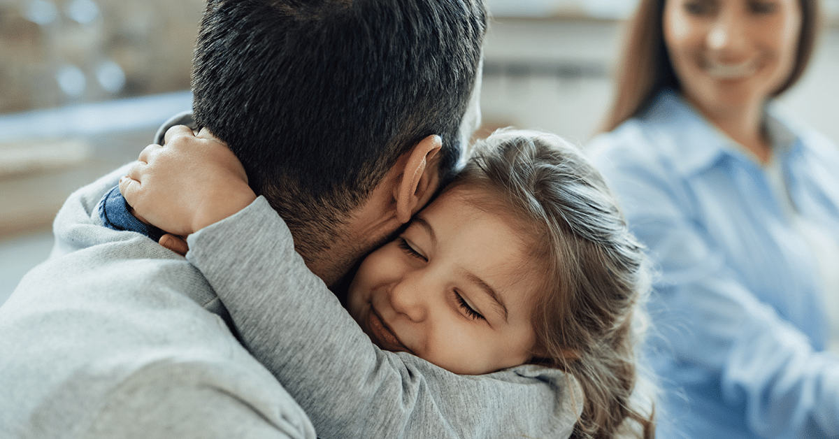 A young daughter embraces her father with a joyful expression, while her mother smiles in the background, watching the tender moment. Family Law Settlement Lawyers in Michigan.